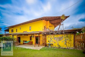 Casa de Alto Padrão em Serra Grande, Bahia – Luxo e Exclusividade com 4 Suítes. Imagine-se vivendo em um lugar mágico, onde cada detalhe foi pensado para proporcionar bem-estar e exclusividade! Este imóvel charmoso, com sua fachada amarela vibrante e detalhes rústicos que encantam, é muito mais do que uma casa; é um estilo de vida cheio de personalidade e boas energias.